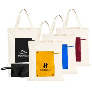 Cotton canvas tote bags standing in a row, each folding into a coloured pouch panel in black, yellow, blue or dark red, printed with logos.