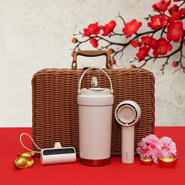 Rattan suitcase basket beside a white thermos flask, a handheld fan and a power bank on red cloth with cherry blossoms