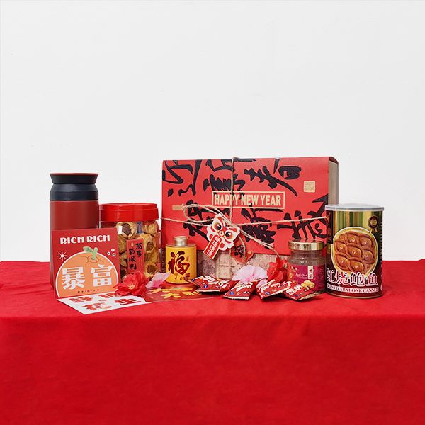 Black thermos flask, red festive gift box, jars of snacks and canned items arranged on a red tablecloth