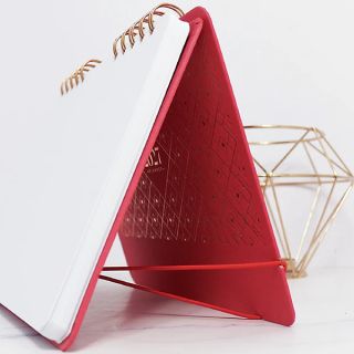 Red desk calendar seen from behind, standing in a tent shape on its board easel beside a gold ornament.