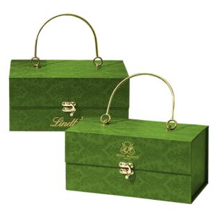 Two green fabric covered handheld boxes with gold handles and clasps, each printed with a logo