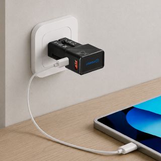 Adapter plugged into a white wall socket, charging a tablet on a wooden table through a white cable.