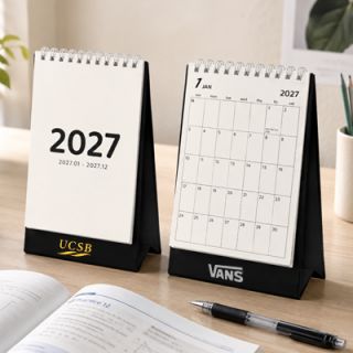 Two Plan Your Days desk calendars on a desk, one closed at the cover and one open at a monthly page