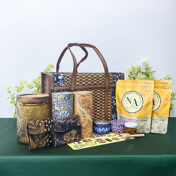 Batik print tins, snack pouches and batik cards spread around a rattan tote basket on a green tablecloth