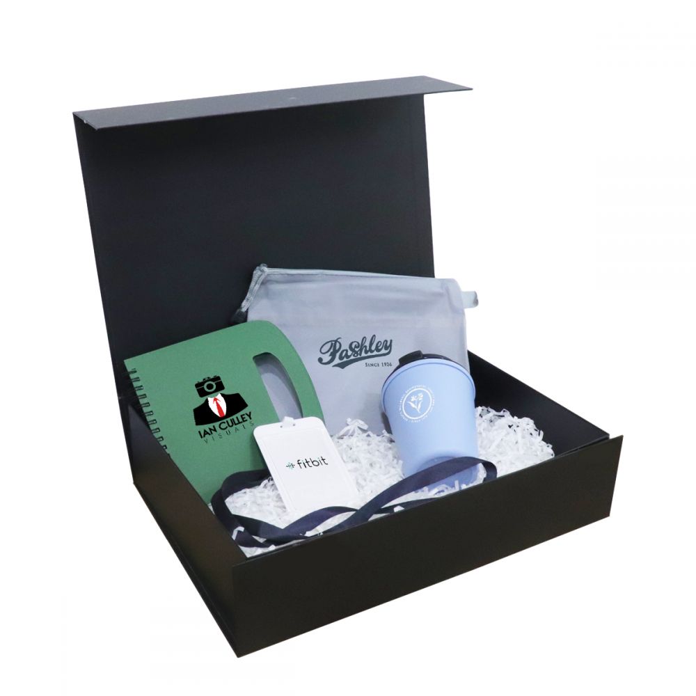 Black magnetic gift box open to show a green notebook, a white tumbler, a pen and a lanyard on shredded paper